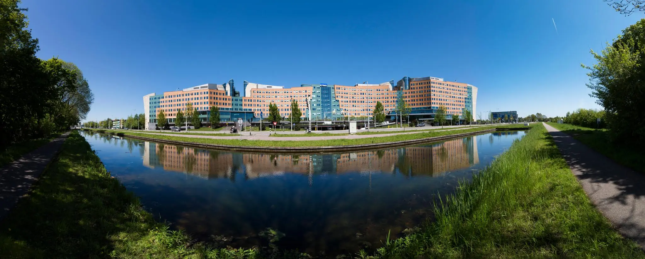 Panoramisch uitzicht op het kantoorcomplex van KPMG aan de Laan van Langerhuize in Amstelveen, weerspiegeld in het water van een naastgelegen kanaal.